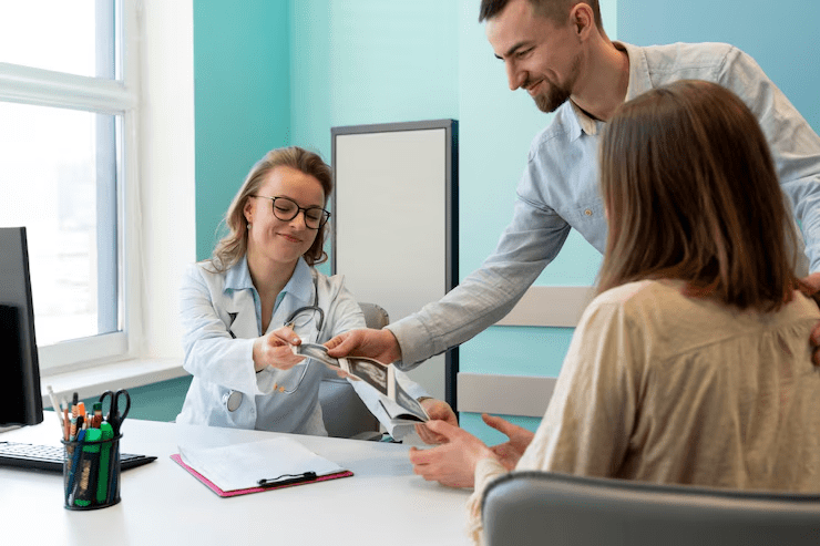 Smiling doctor receiving cash payment from a couple during a health consultation in a medical office, representing out-of-pocket expenses and private healthcare services.