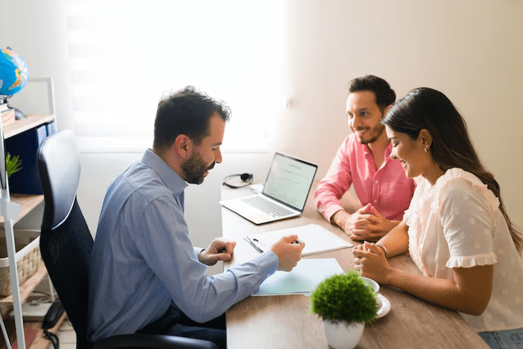 Smiling couple meeting with a financial advisor in a bright office, reviewing documents and discussing financial planning or investment options with a laptop open on the desk.