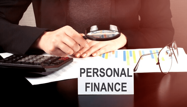 Close-up of a person analyzing financial charts with a magnifying glass and calculator, next to a card labeled "Personal Finance," symbolizing careful budgeting, financial planning, and money management.