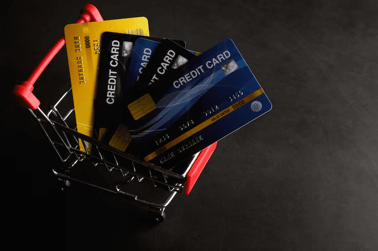 "Miniature shopping cart filled with various credit cards on a dark background, symbolizing financial choices, credit card shopping, or consumer spending."