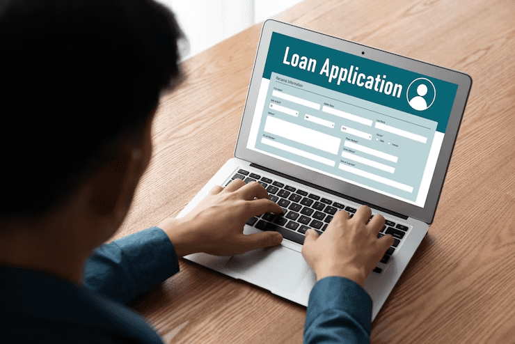 "Man filling out an online loan application form on a laptop, seated at a wooden table, indicating the digital process of applying for a financial loan."