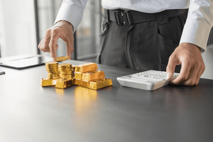 Businessman managing stacks of gold coins and gold bars next to a computer keyboard on a desk, representing the concept of understanding gold loans, asset-backed borrowing, and financial planning.