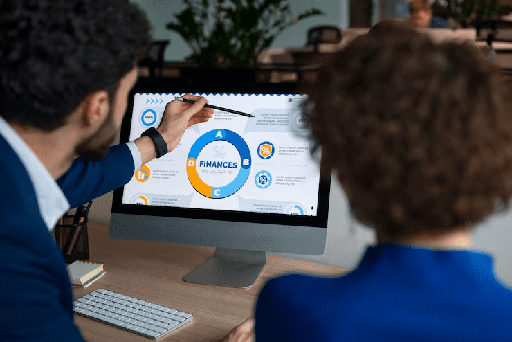 A man and a woman in business attire analyzing a financial infographic on a desktop screen, with the word “Finances” at the center—symbolizing financial planning, data analysis, or investment strategy discussions.