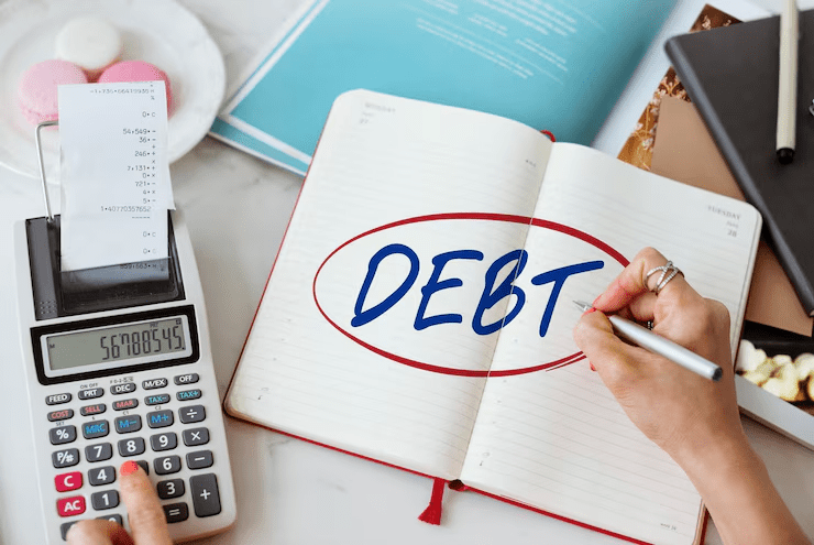 Person using a calculator and writing the word "DEBT" in a notebook, emphasizing financial planning or debt management.