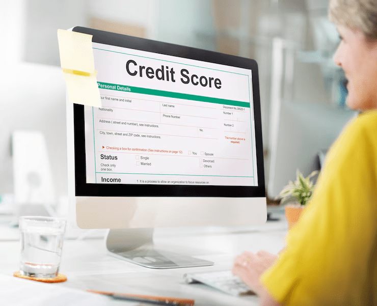 A woman using a desktop computer displaying a credit score application form, with sections for personal details, income, and marital status, in a bright office setting.