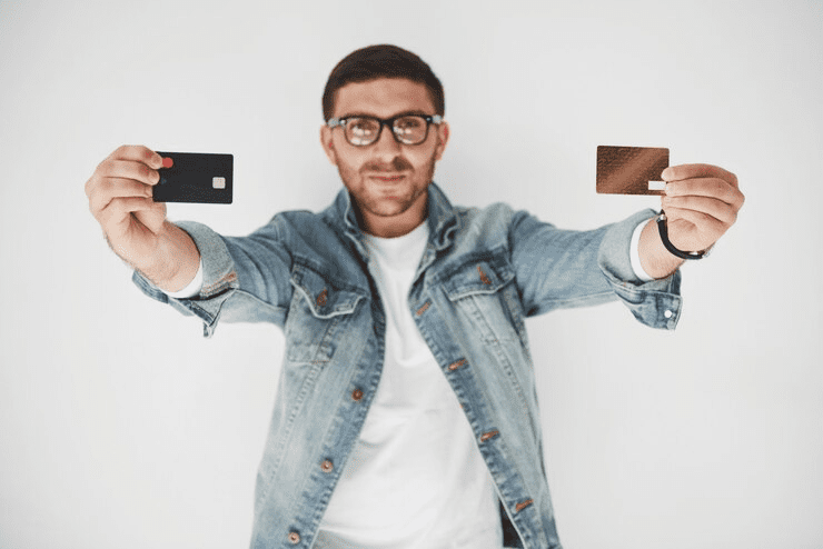  Man wearing glasses and a denim jacket holding two different credit cards toward the camera, representing major cashback credit cards comparison for selecting the best rewards and benefits.