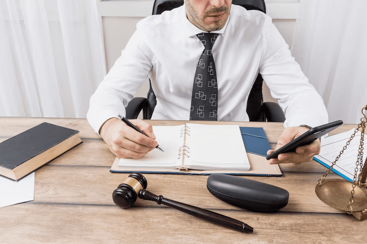 Lawyer or legal professional sitting at a desk with a notebook, smartphone, gavel, and justice scales, symbolizing legal work, case planning, and decision-making in a professional law environment.